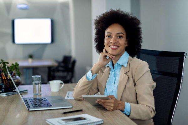 Happy black entrepreneur working at wedding Dj managed event service at her office desk and looking at camera.